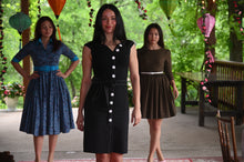 Load image into Gallery viewer, A woman wearing a fitted black pencil dress with white buttons, standing confidently in a modern setting. The dress is sleek, elegant, and flattering, blending business and style.
